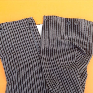May include: A pair of black and white striped pants with a zipper and buttons. The pants are folded in half and the fabric is textured.