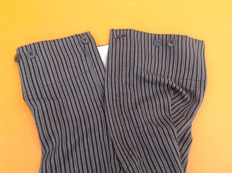 May include: A pair of black and white striped pants with a zipper and buttons. The pants are folded in half and the fabric is textured.