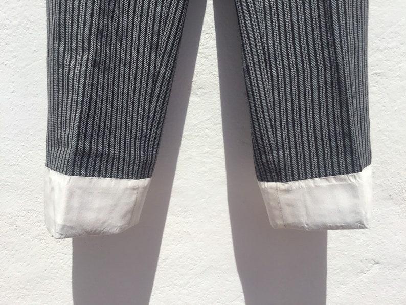 May include: A pair of black and white striped pants with white cuffs. The pants are made of a lightweight fabric and have a relaxed fit.