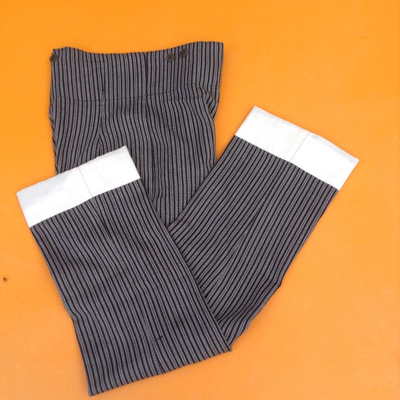 May include: A pair of black and white striped pants with white cuffs. The pants have a button closure at the waist.