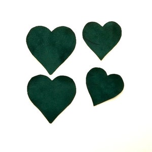 May include: Four dark green felt heart shapes on a white background.
