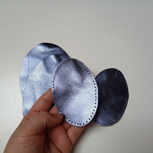 Puede incluir: Tres piezas de cuero ovaladas en tonos azules y morados. El cuero es texturizado y tiene un brillo sutil. Las piezas están dispuestas en una pila, con la pieza más grande en la parte inferior y la más pequeña en la parte superior.