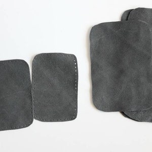 Peut inclure: Plusieurs pièces de cuir gris foncé sont disposées sur une surface blanche. Deux petites pièces ont des bords cousus, tandis que les plus grandes sont lisses. Les pièces de cuir sont rectangulaires avec des coins arrondis.
