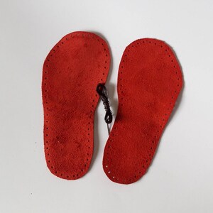 May include: Two red leather soles with a black thread running through the holes around the edges.