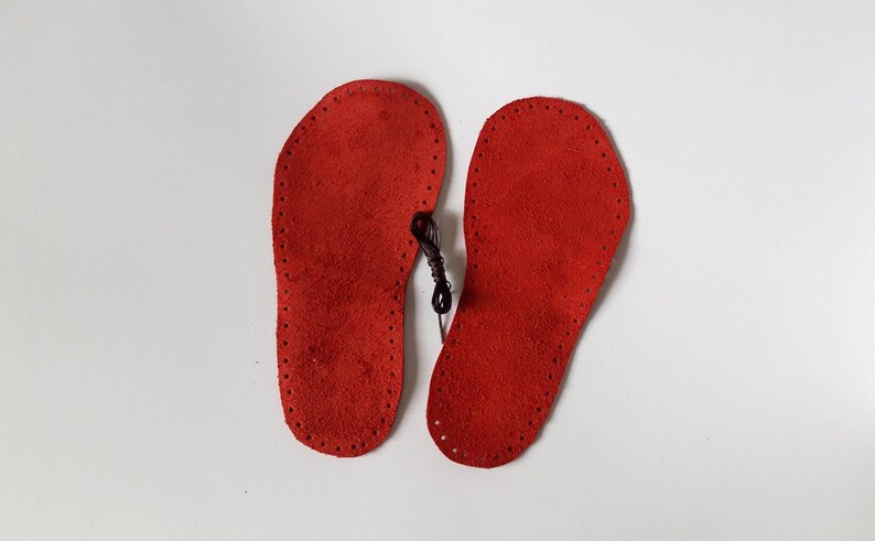 May include: Two red leather soles with a black thread running through the holes around the edges.