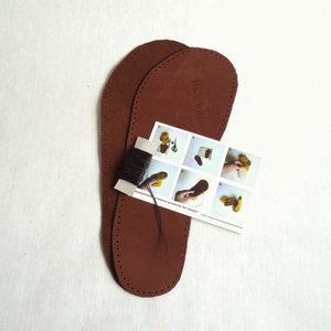 May include: Two brown leather soles for making moccasins. The soles are pre-punched with holes for stitching. A small instruction card with illustrations shows how to sew the moccasins. The card says "handmade creative products for family".