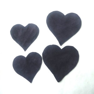 May include: Four black felt hearts on a white background.
