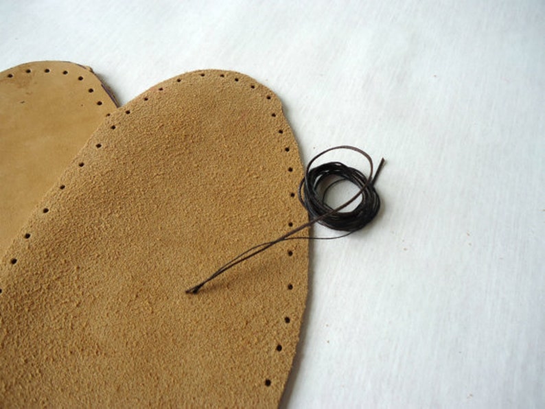 May include: Two pieces of brown leather with holes punched around the edges. A spool of brown thread is on the right side of the image.