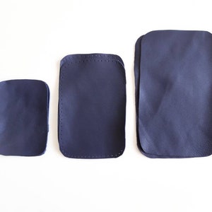 May include: Three different sizes of dark blue leather patches. The patches are rectangular and have a stitched edge.