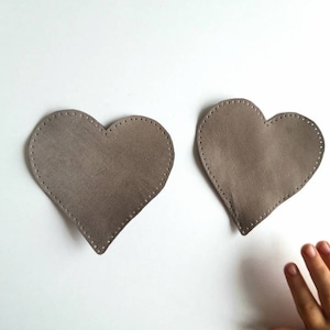 May include: Two brown felt heart shapes on a white background.
