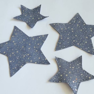 Peut inclure: Quatre étoiles en tissu gris avec des pois blancs. Les étoiles sont de tailles différentes et sont disposées en quinconce.