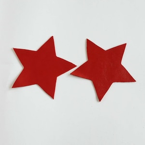 May include: Two red felt stars on a white background.