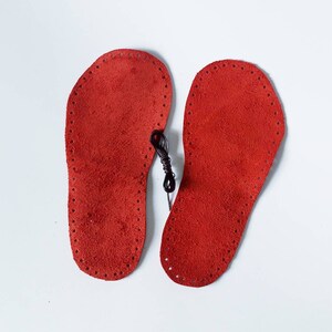 May include: Two red leather insoles with a black thread running through the holes around the edges.