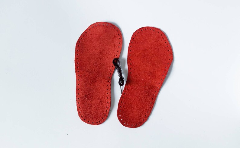 May include: Two red leather insoles with a black thread running through the holes around the edges.