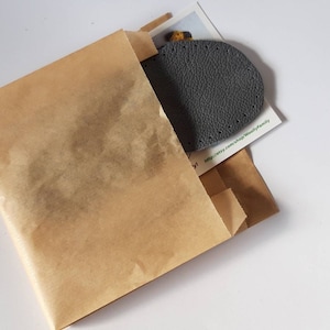 May include: A gray leather patch with stitching around the edges is packaged in a brown paper envelope.