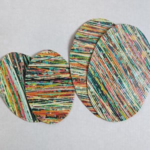 Può includere: Quattro sottobicchieri ovali con un motivo a strisce colorate. I sottobicchieri sono realizzati in un materiale che ricorda il legno o il sughero.