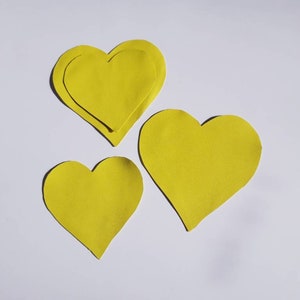 May include: Three yellow felt hearts of different sizes. The hearts are arranged in a triangular shape on a white background.