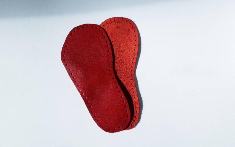 May include: Two red leather insoles with a stitched edge and holes along the edge.