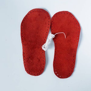 May include: Two red leather insoles with white stitching around the edges. A spool of white thread is in the center of the image.