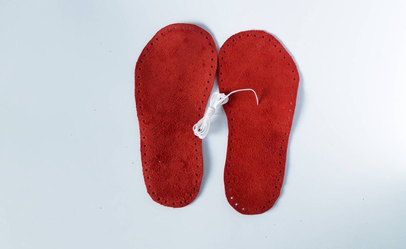 May include: Two red leather insoles with white stitching around the edges. A spool of white thread is in the center of the image.