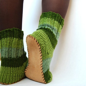 May include: A pair of green and brown striped knitted socks with leather soles. The socks are worn on a person's feet.