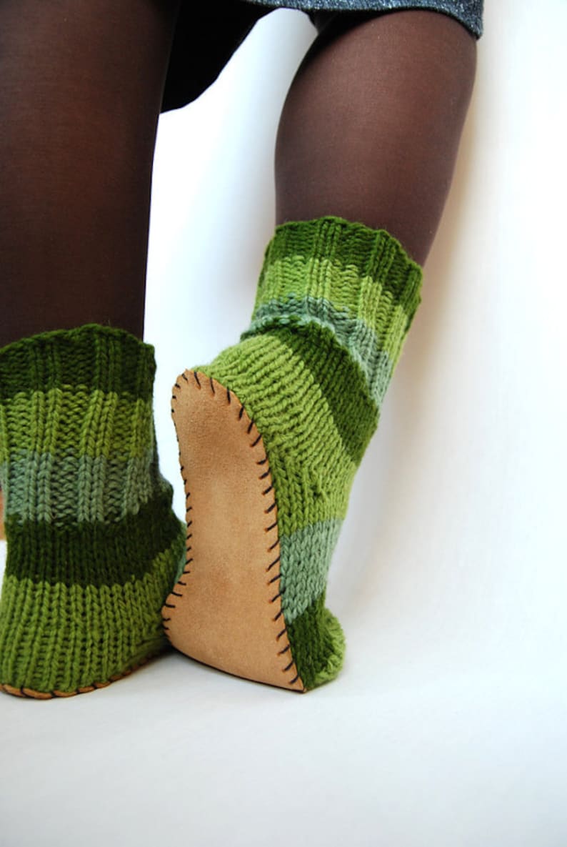 May include: A pair of green and brown striped knitted socks with leather soles. The socks are worn on a person's feet.