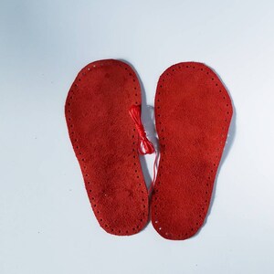 May include: Two red leather soles with holes around the edges, ready to be sewn together.