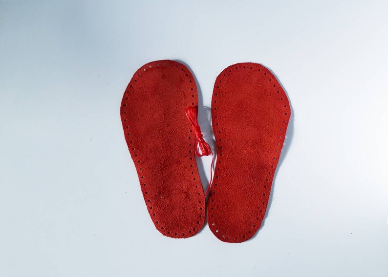 May include: Two red leather soles with holes around the edges, ready to be sewn together.