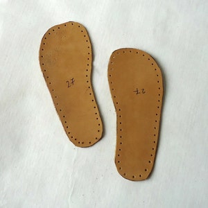 May include: Two brown leather shoe soles with holes around the edges. The soles are labeled "27" and "72".