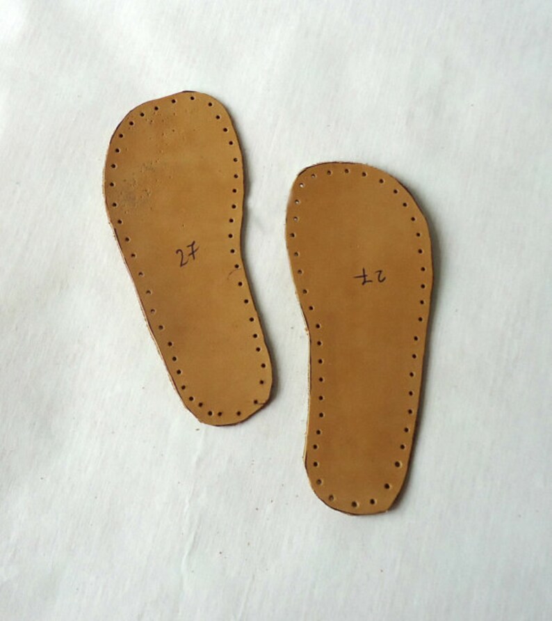 May include: Two brown leather shoe soles with holes around the edges. The soles are labeled "27" and "72".