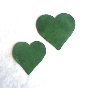 Peut inclure: Deux formes de cœur en feutre vert, l'une plus grande que l'autre, sur un fond blanc.