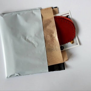 May include: A white padded envelope with a brown paper envelope inside. The brown envelope contains a red leather patch with stitching around the edges.