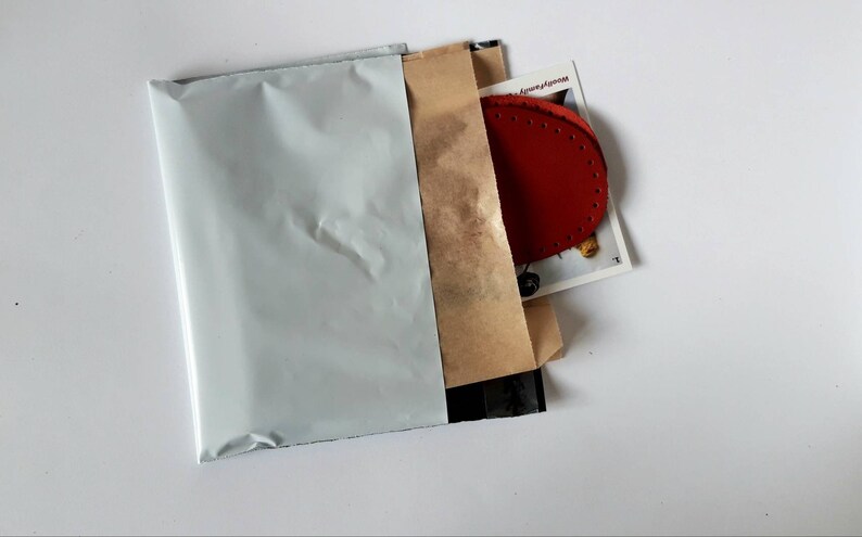 May include: A white padded envelope with a brown paper envelope inside. The brown envelope contains a red leather patch with stitching around the edges.