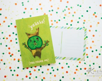 May include: A green postcard with a cartoon illustration of a tree with a face and the text "yahaha! (you found me)". The postcard has a white border and is surrounded by green and orange confetti.