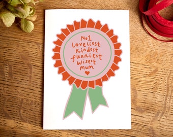 May include: A white card with a red and green rosette with the text "No1 loveliest kindest funniest wisest mum" inside the rosette.