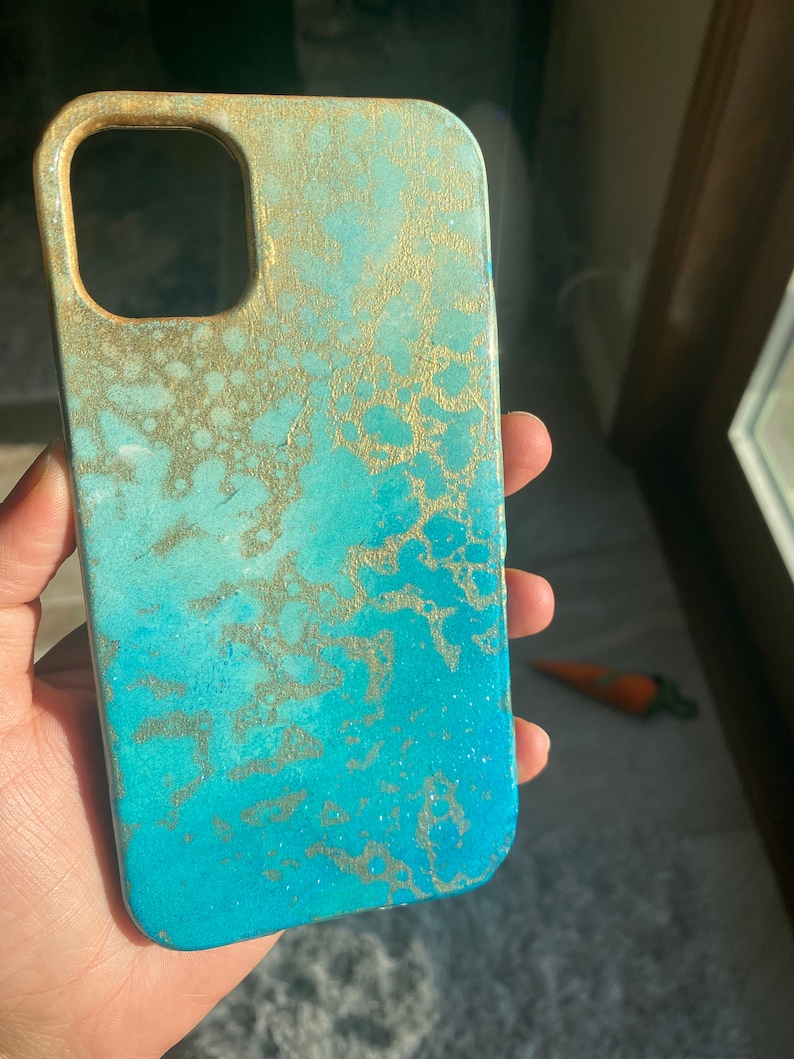 May include: A blue and gold phone case with a marbled design. The case has a raised edge around the camera lens.