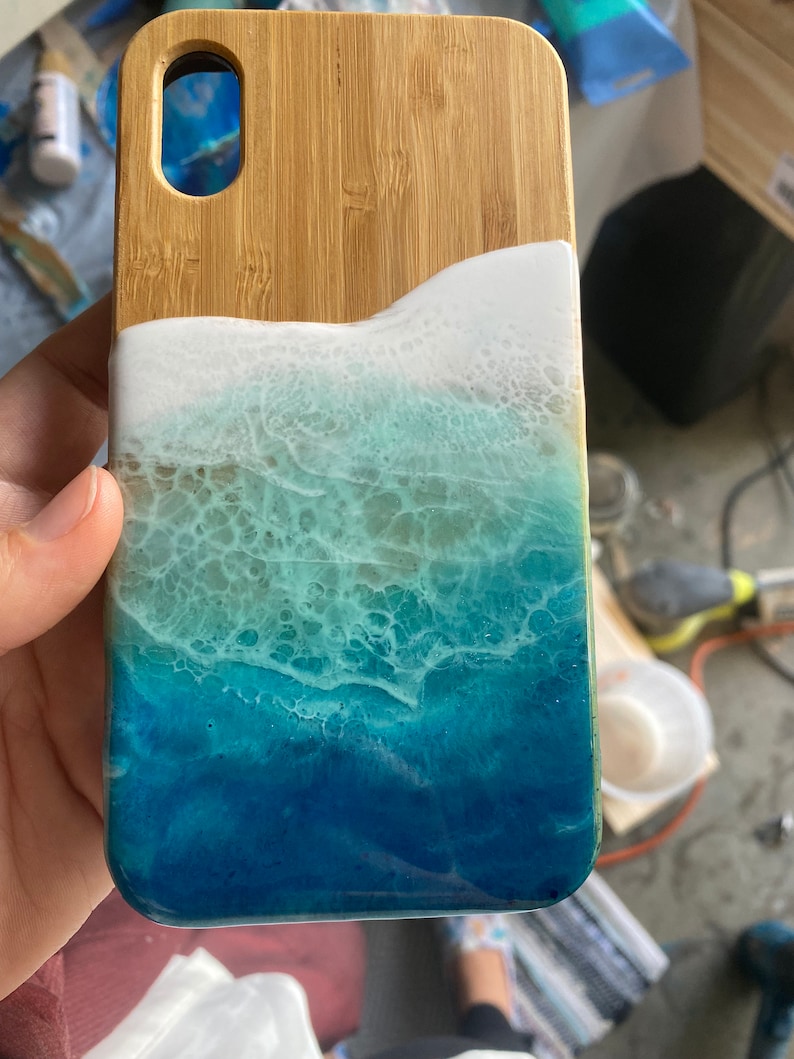 May include: A phone case made of wood and resin with a blue and white ocean wave design.