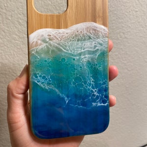 May include: A wooden phone case with a blue, green, and white resin ocean wave design.