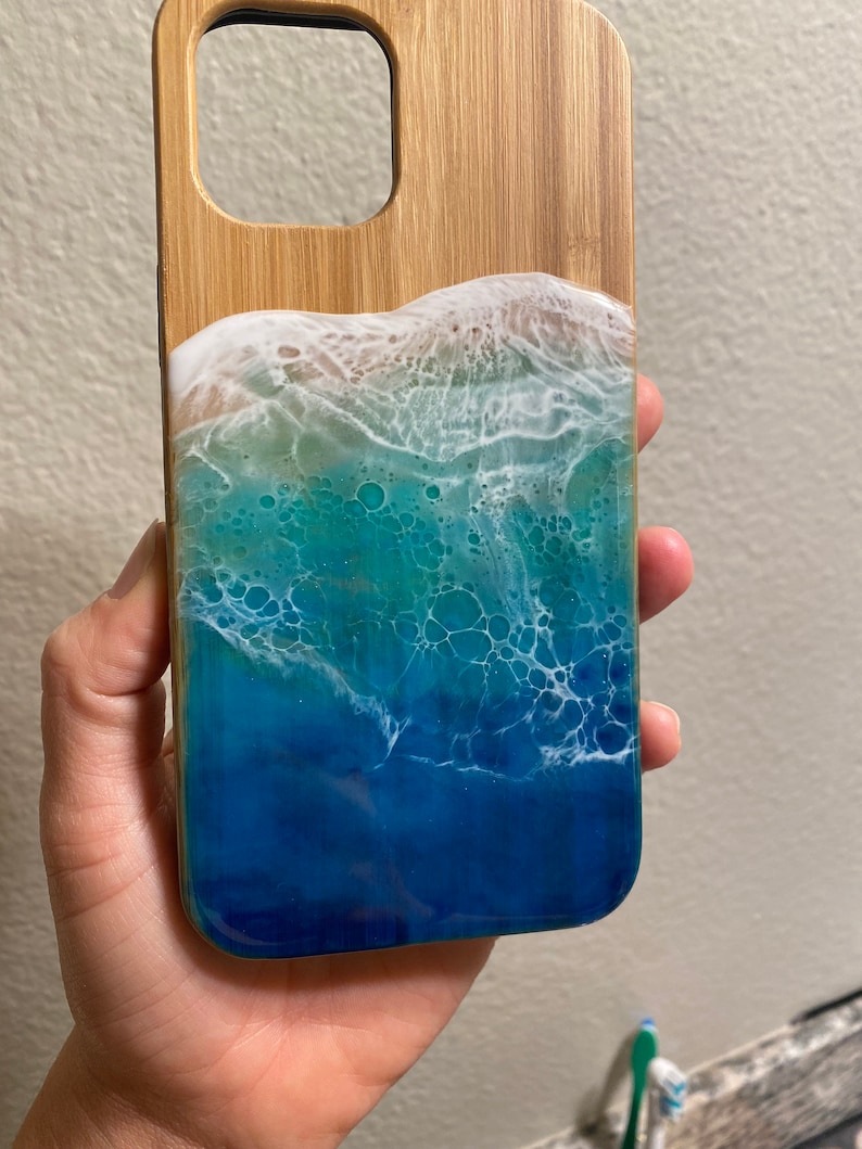 May include: A wooden phone case with a blue, green, and white resin ocean wave design.