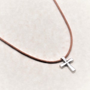 May include: A silver cross pendant on a brown leather cord necklace.