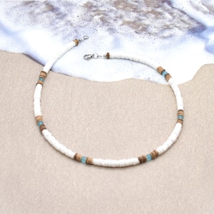 May include: A white and brown beaded necklace with light blue accents. The necklace is made of small, round beads and has a silver clasp.