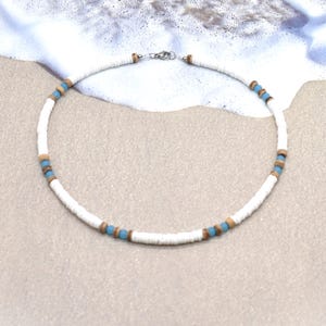 May include: A beaded necklace featuring a repeating pattern of flat white disc beads, small round light blue beads, and small round brown wooden beads. The necklace is secured with a silver-toned metal clasp at the top, creating a circular shape.