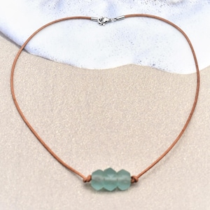 May include: A light brown leather cord necklace with a cluster of three light blue sea glass beads.