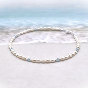 May include: A delicate white pearl and light blue gemstone bracelet. The bracelet is made with small, round pearls and tiny blue gemstones.