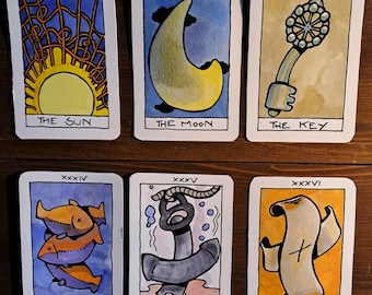 May include: Six rectangular tarot cards with hand-drawn illustrations and black borders. The cards feature a yellow sun, a crescent moon, a decorative key, three orange fish, a grey anchor with rope, and a scroll with a cross, labeled XXXI to XXXVI.