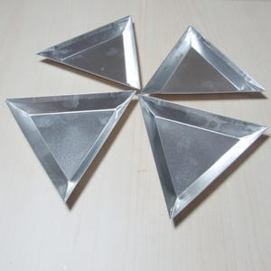 May include: Four silver triangular trays arranged in a circular pattern on a light wood surface.