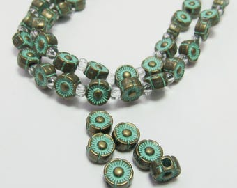 May include: Close-up of a necklace and loose beads. The beads are a bronze color with a turquoise floral design. The necklace is strung with clear beads. The beads are small and round, with a detailed floral pattern.
