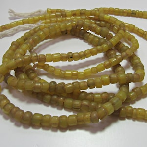 May include: A strand of yellow glass beads, each bead is square shaped with rounded edges. The beads are strung on a white cord.