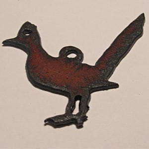 May include: A metal cutout of a roadrunner, a desert bird, with a rusty brown patina. The cutout is black and has a hole at the top for hanging.