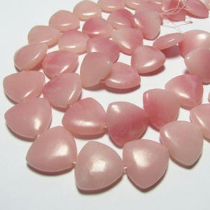 May include: A collection of pink heart-shaped beads. The beads are strung together, showcasing a variety of shades from light to darker pink. The smooth, polished surface of each bead reflects light, creating a subtle sheen.